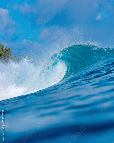 Massive blue ocean wave curling, bright turquoise barrel breaking with foamy crest and spray, sunlight