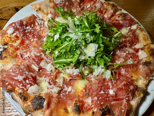 Rustic Wood Oven Pizza with Prosciutto, Arugula, and Parmesan Cheese on White Plate