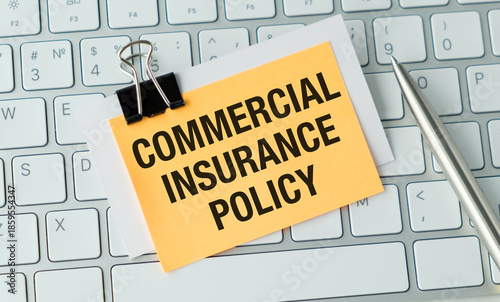 A yellow piece of paper with the words COMMERCIAL INSURANCE POLICY written on it. A pen is sitting on top of the paper