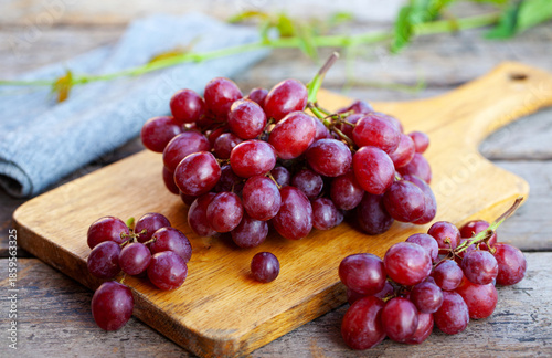 Fresh red grapes cluster on cutting board. Rustic wooden background. Close up.