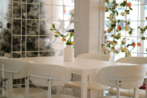 Modern dining area featuring a minimalist white table with stylish chairs, decorative vase, and floral accents in a bright and inviting environment