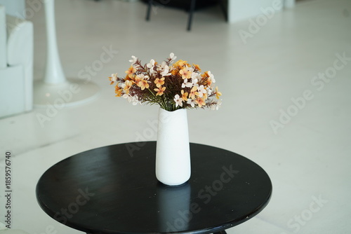 Elegant arrangement of artificial flowers in a minimalist white vase on a black table in a well-lit modern indoor setting