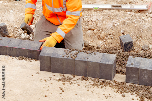 Foto Construction worker laying key kerb paving blocks on a building site