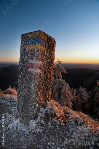 überfrorener Granitpfeiler mit Wegweisermarkierungen beim Sonnenuntergang