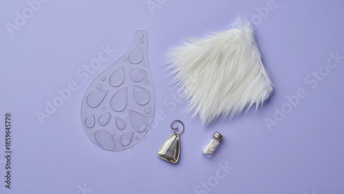 Artistic Still Life Composition Featuring a Teardrop Shaped Template, Faux Fur Piece, Small Bell, and Tiny Bottle on a Light Purple Background for Crafts