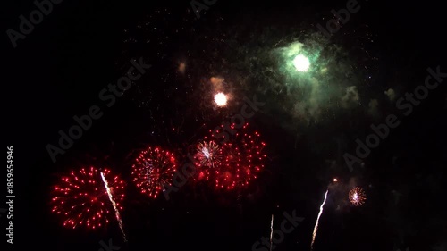 Spectacular nighttime fireworks display with vibrant red green and white bursts illuminating the dark sky