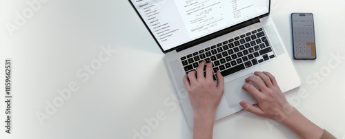 High angle view of student hands typing on laptop computer displaying algebra problems next to smartphone calculator app on white table with large empty space for text or design placement