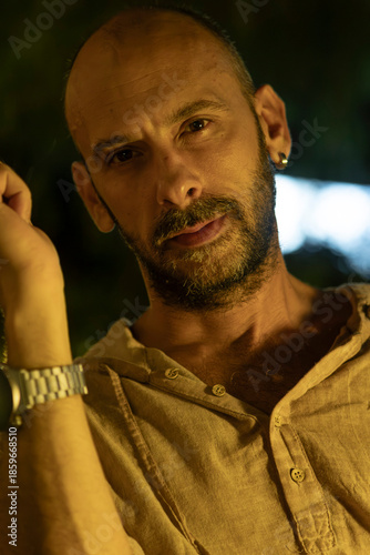 A portrait of a mature man sitting at a cozy outdoor cafe table during a warm summer evening, enjoying a cup of coffee. He looks relaxed and thoughtful in a modern urban lifestyle setting.