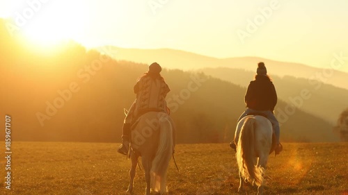 Two women riding horses toward the sunset across an open meadow, calm atmosphere and shared equestrian freedom