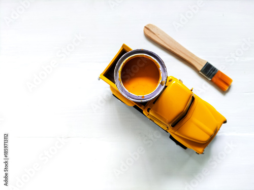 A small yellow toy truck holds a tin of yellow paint in its bed, suggesting car repaint concept.