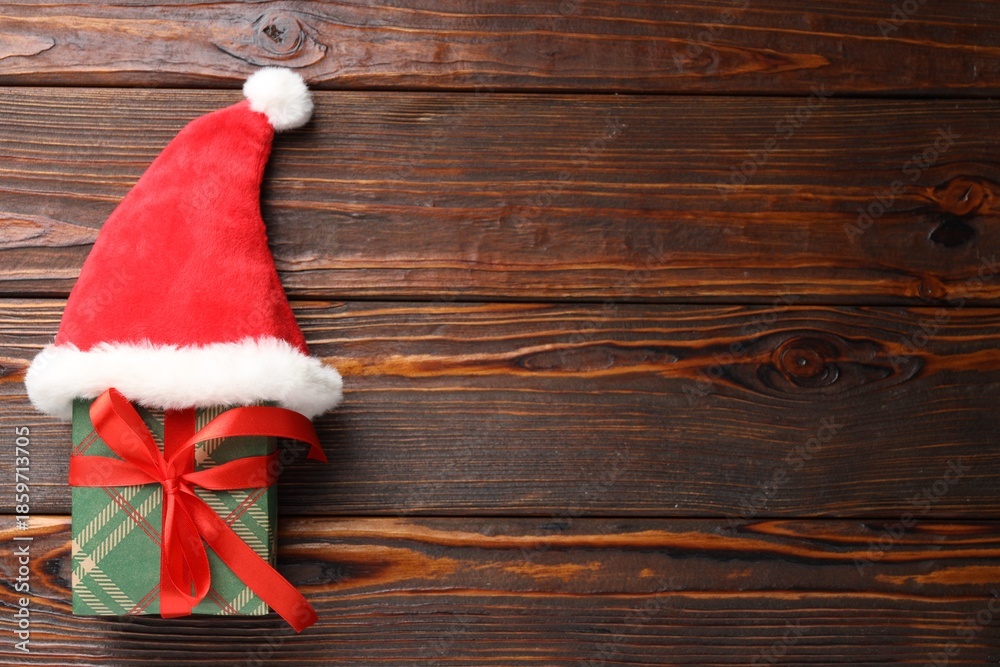 Fototapeta premium Christmas gift with Santa hat on wooden table, top view. Space for text