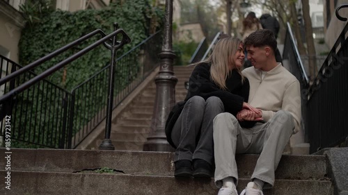 A young couple in love sits on the steps in Montmartre Paris They are holding hands and smiling at each other enjoying a romantic moment in the city The scene captures a sense of togetherness and happ