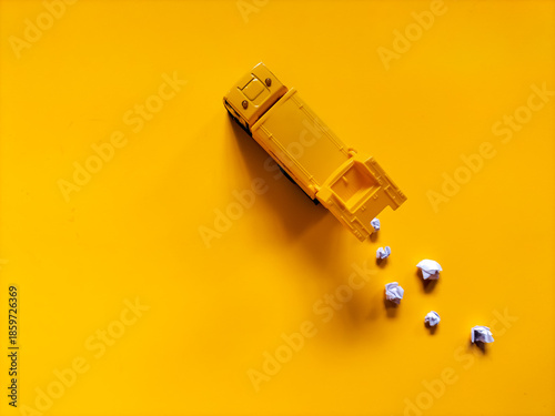 Yellow toy garbage truck positioned diagonally on a matching yellow background. 