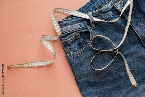 Concept of diet, weight loss, healthy eating. Blue jeans with a measuring white tape around the waist on a pink background.