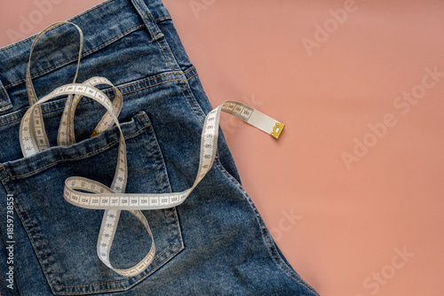 Concept of diet, weight loss, healthy eating. White measuring tape in the back pocket of blue jeans on a pink background.