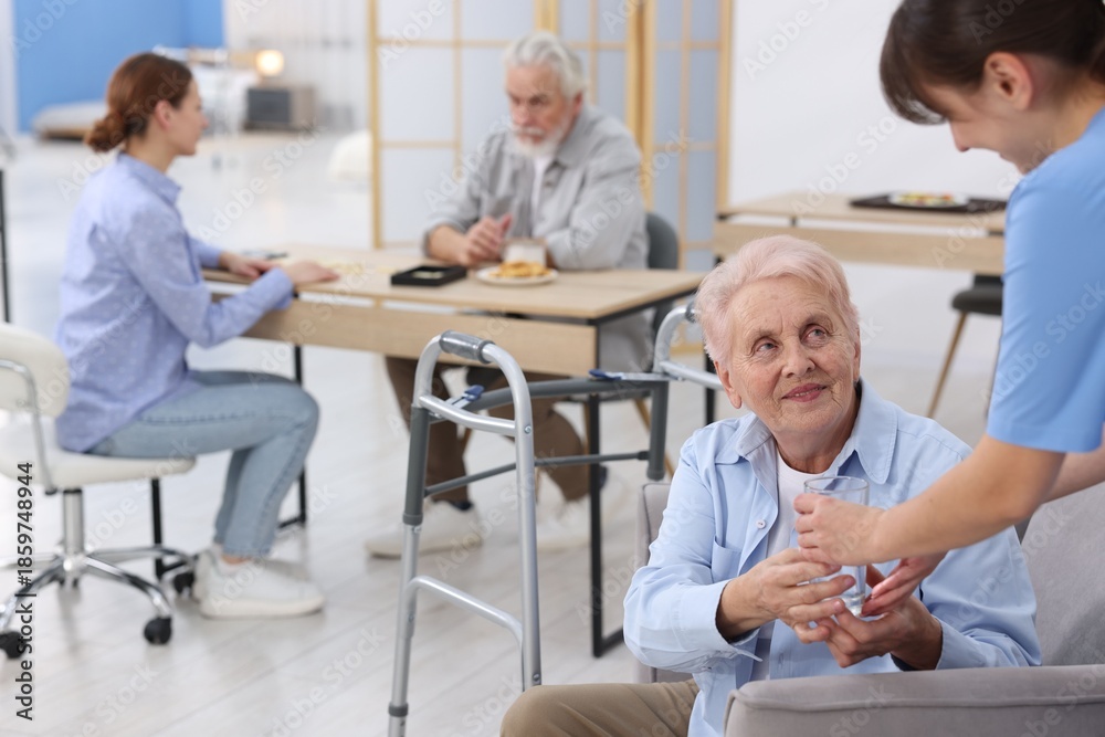 Fototapeta premium Care worker giving glass of water to senior woman at retirement home