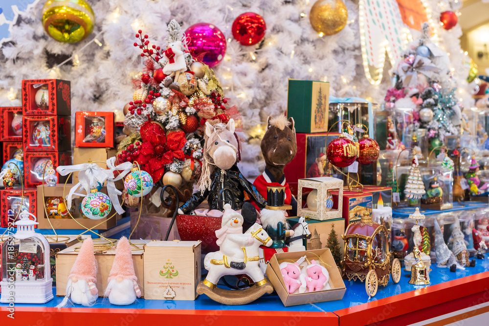 Naklejka premium Moscow, Russia,A vibrant Christmas market stall displaying various holiday decorations, including stuffed animals, snow globes, and rocking horses, against a backdrop of a white Christmas tree.