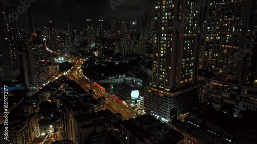 An aerial view of Mumbai's high-rise buildings and beautiful nightlights. The sky is cloudy, and there is medium traffic on the road. The cityscape is filled with modern illuminated buildings.