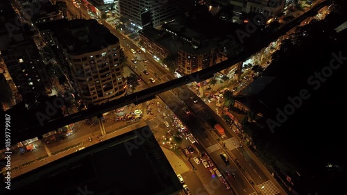 An aerial view of Mumbai's high-rise buildings and beautiful nightlights. The sky is cloudy, and there is medium traffic on the road. The cityscape is filled with modern illuminated buildings.