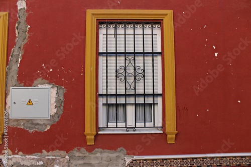 Fényképezés Traditional barred window with decorative wrought iron grille on red stucco faca