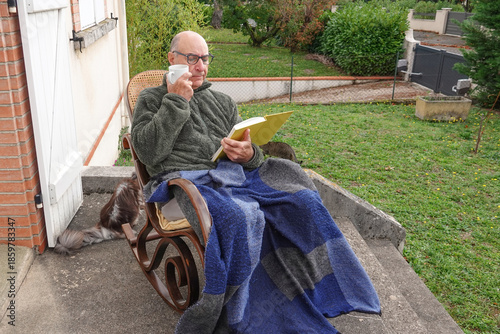 senior man enjoys reading a book and sipping a drink in his yard