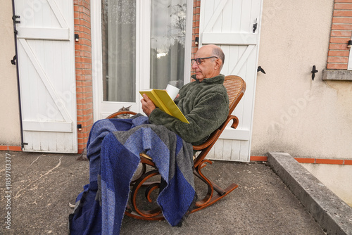 retired man enjoys reading on a rocking chair outside a house