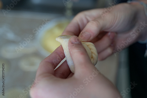 Close-up of hands carefully shaping dumpling dough with a braided edge. Homemade cooking process with selective focus, showing texture, tradition, and cooking at home atmosphere.