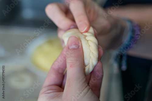 Close-up of hands carefully shaping dumpling dough with a braided edge. Homemade cooking process with selective focus, showing texture, tradition, and cooking at home atmosphere.