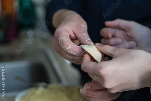 Elderly hands help child's hands fold dumpling dough near kitchen sink, selective focus on flour-dusted fingers in cooking at home with grandma, authentic family tradition