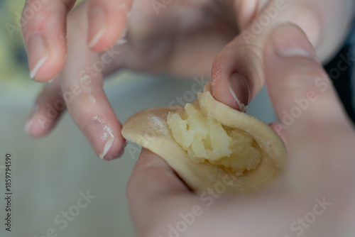 Close-up of hands filling dumpling dough with mashed potato stuffing. Traditional homemade cooking with selective focus, soft focus background, and authentic cooking at home mood.