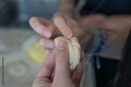 Close-up of hands carefully shaping dumpling dough with a braided edge. Homemade cooking process with selective focus, showing texture, tradition, and cooking at home atmosphere.