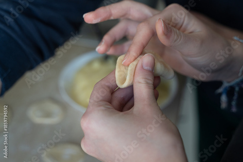 Close-up of hands filling dumpling dough with mashed potato stuffing. Traditional homemade cooking with selective focus, soft focus background, and authentic cooking at home mood.
