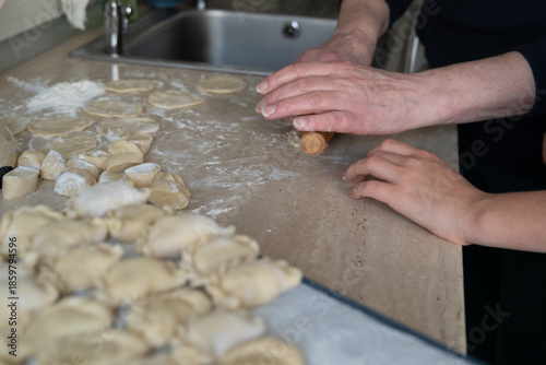 Hands of an older woman and child making dumplings together in a home kitchen. Warm family moment with homemade food, selective focus, and cozy cooking with grandma atmosphere.