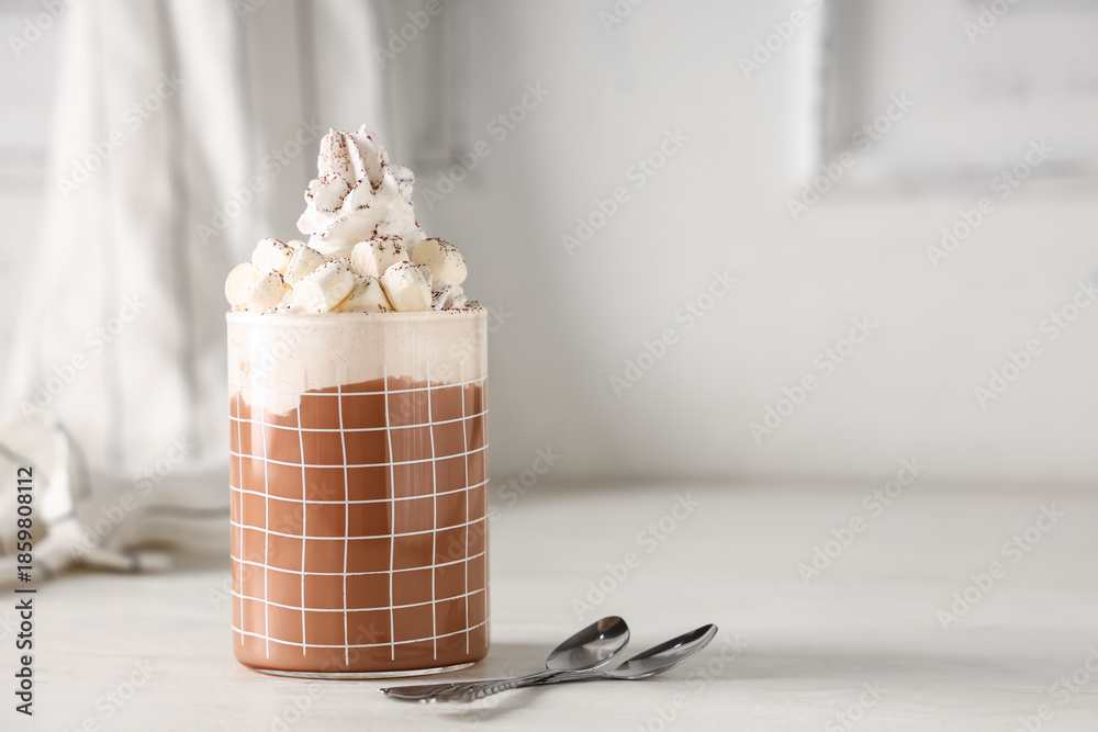 Fototapeta premium Glass of hot cocoa drink with whipped cream and marshmallows on white wooden table