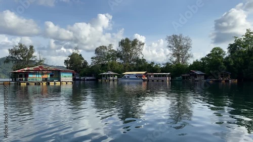 Traditional Bajo tribe stilt houses built over crystal clear sea water. Scenic coastal village of sea gypsies with green hills and blue sky reflections in Central Sulawesi, Indonesia.
