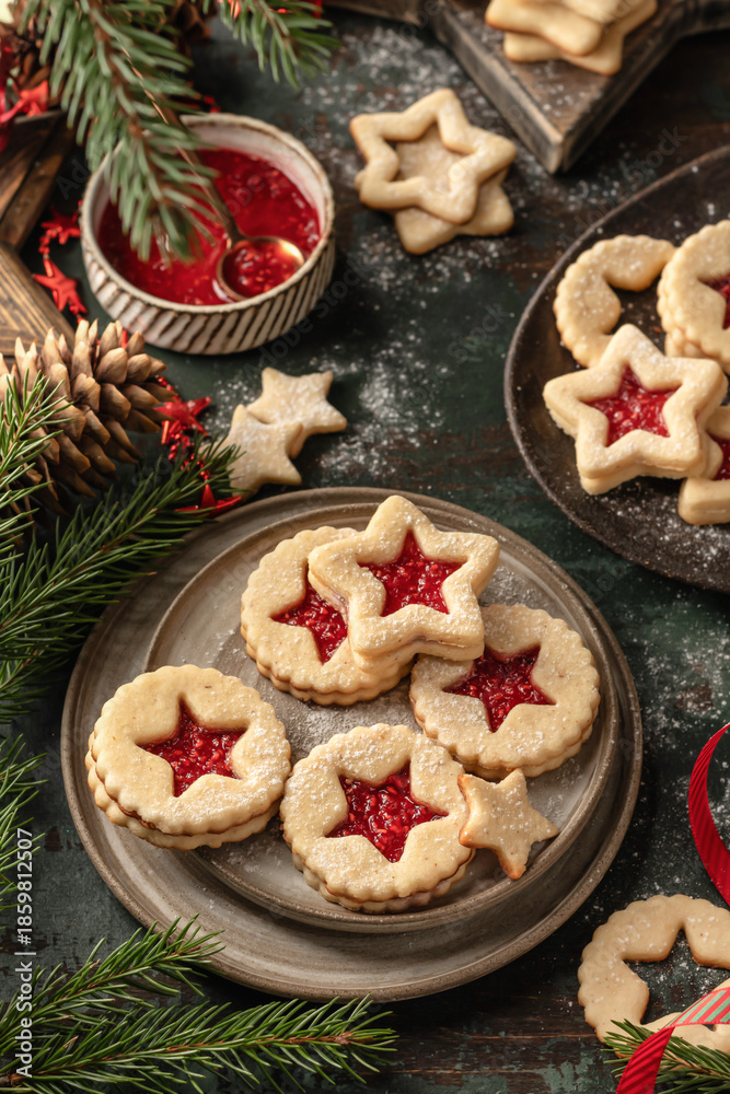 Fototapeta premium Homemade Linzer Christmas cookies filled with raspberry jam and dusted with sugar on ceramic plate with fir tree branches and festive decorations
