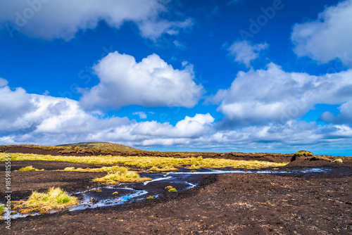 Eroded peatland landscape with exposed dark soil and isolated peat ‘islands’ under a bright blue sky