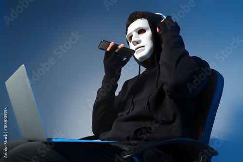 Bilde på lerret Male fraudster in headphones with laptop talking by mobile phone on light backgr