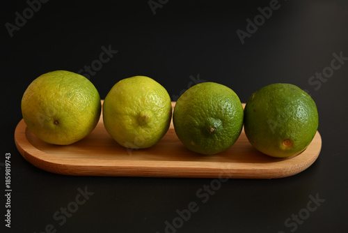 Vibrant whole green limes on a wooden board. Minimalist studio composition over a dark background, perfect for culinary and wellness concepts.
