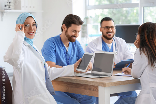 Female Muslim doctor working with tablet computer and colleagues at table in ...