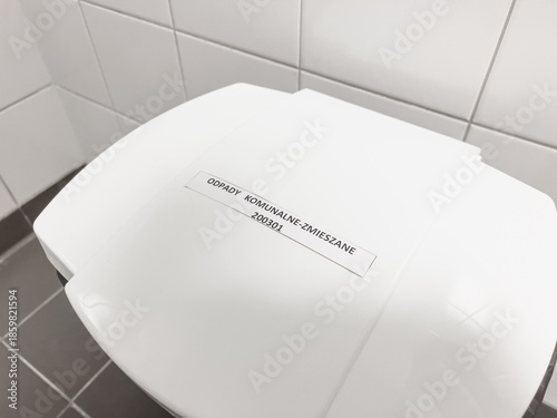 Modern white plastic waste bin mixed with Polish label on gray tiles in bright sterile interior horizontal orientation photos 