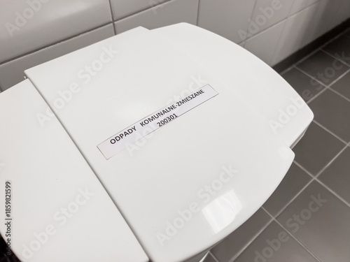 Modern white plastic waste bin mixed with Polish label on gray tiles in bright sterile interior horizontal orientation photos 