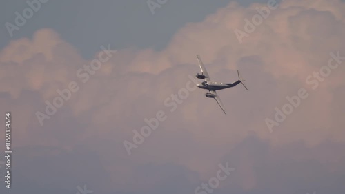 Twin engine turboprop aircraft flying level against cloudy sky with warm sunset lighting during cruising phase
