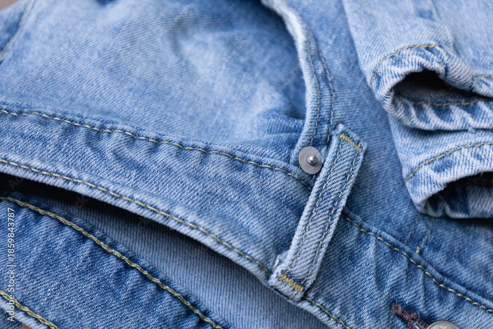 Naklejka premium Blue Denim Jeans Fabric Texture.Close-up of blue denim jeans fabric with visible seams and stitching, showing texture, folds, and worn cotton material detail for fashion or textile concepts.
