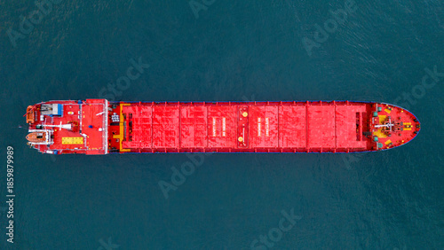 Top down panoramic view of a massive red cargo ship sailing vertically in the frame emphasizing the scale of the vessel against the deep blue ocean water texture