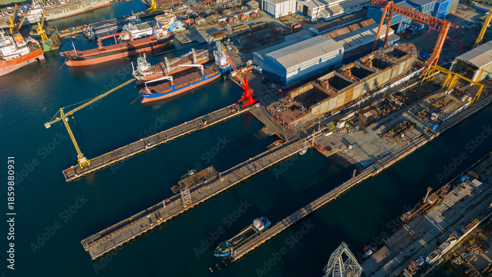 Obraz premium Aerial view of large yellow cranes standing on the pier of a shipyard ready to lift heavy loads for ship repair and construction projects in a sunny industrial setting