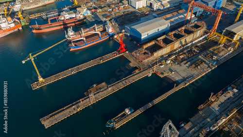 Aerial view of large yellow cranes standing on the pier of a shipyard ready to lift heavy loads for ship repair and construction projects in a sunny industrial setting