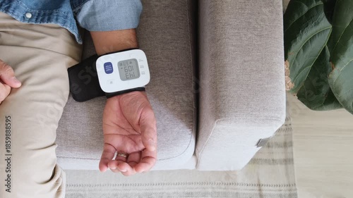 Unrecognizable man using a digital tonometer to measure his blood pressure while sitting on a sofa