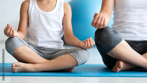 Child and adult practicing yoga together in a calm indoor setting, seated in lotus position on a blue mat
