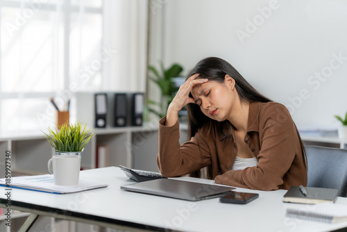 Photos Overwhelmed in the Office: A professional experiences a moment of stress while working, hand on head, in her office